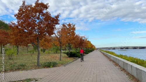 Cyclist riding bicycle on waterfront promenade with autumn trees river view and bridge during fall season