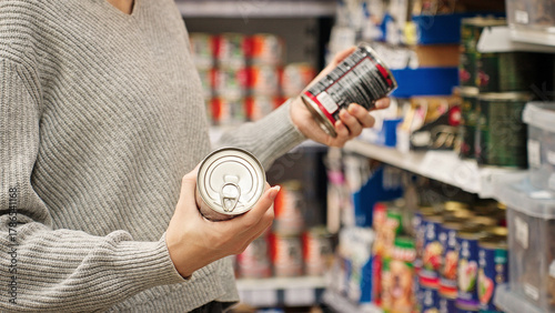A woman choosing canned dog or cat food at a pet store, reading the label. Customer compares wet dog or cat food in the aisle with various canned goods on the shelves. Concept of responsible pet owner