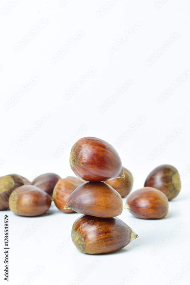 Fototapeta premium Close up, chestnuts stacked on a white background. In vertical.