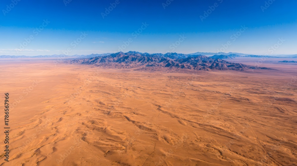 Fototapeta premium Arid desert landscape with distant mountains under a clear blue sky, showing vast empty wilderness aerial view