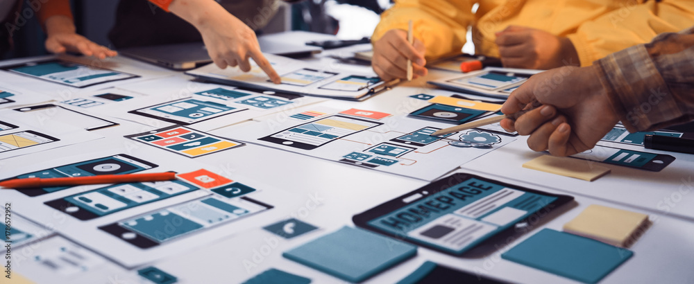 Obraz premium A dynamic team collaborates on mobile app design, engaging with wireframe prototypes and vibrant sketches on the table, fostering creativity and innovation in a workspace. SACTR