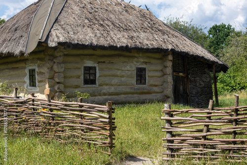 Traditional log cabin with thatched roof and wooden fence in countryside
