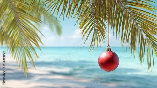 Fototapeta Naklejka Na Ścianę i Meble -  Single red Christmas ornament hanging from palm tree branch. Tropical beach panorama background
