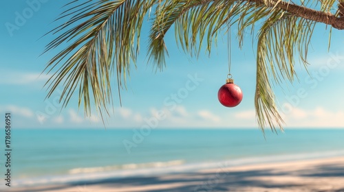 Fototapeta Naklejka Na Ścianę i Meble -  Single red Christmas ornament hanging from palm tree branch. Tropical beach panorama background
