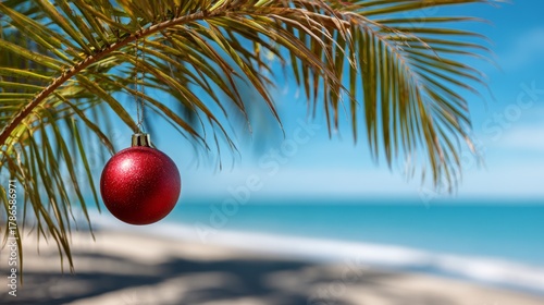 Fototapeta Naklejka Na Ścianę i Meble -  Single red Christmas ornament hanging from palm tree branch. Tropical beach panorama background