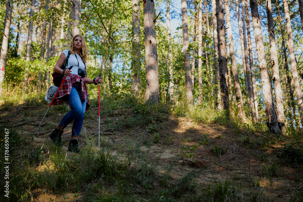 Obraz premium Woman hiking in summer forest using trekking poles