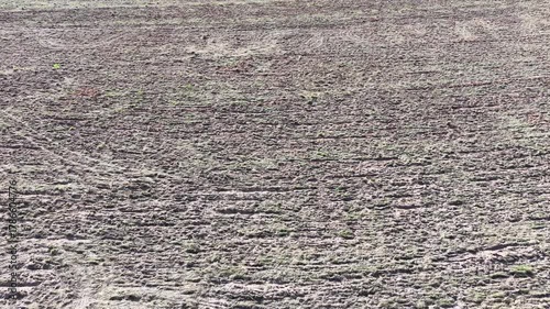 An abstract texture of tilled soil, revealing patterns created by agricultural machinery. The rough surface of the dirt implies work, harvest or barrenness