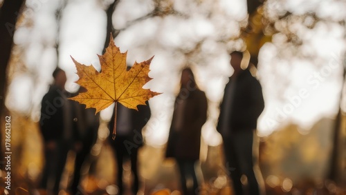 Autumnal Ambience - Maple Leaf in Focus, Blurred Figures in Background.