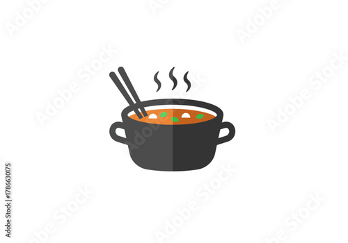 Dark cooking pot of steaming orange soup with chopsticks and whitegreen bits