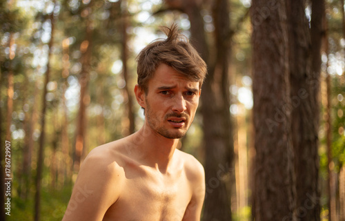 a worried  upset guy in the woods with a bare chest