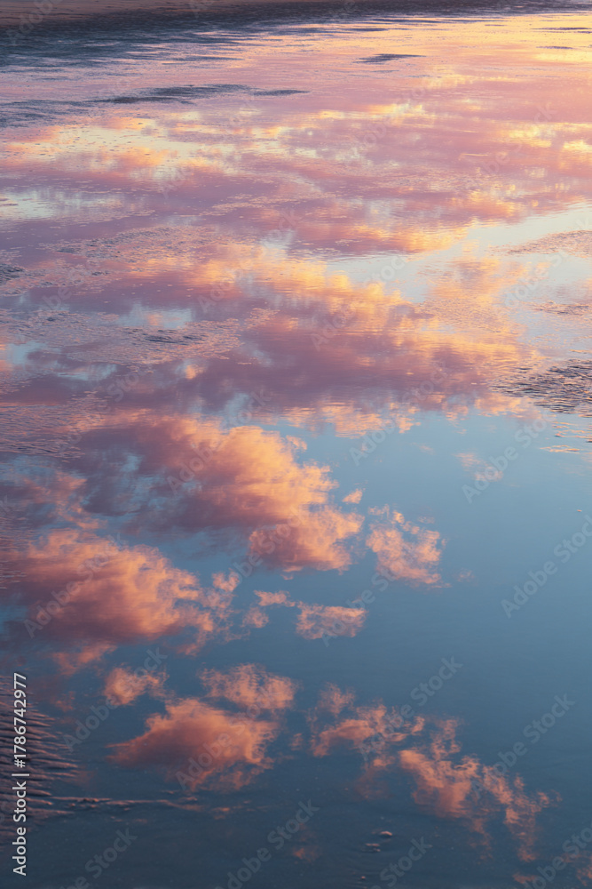 Fototapeta premium Soft Reflections of Sunrise Clouds on Wet Sand, Mirror-Like Shore with Pastel Glow – great for inspirational wall art