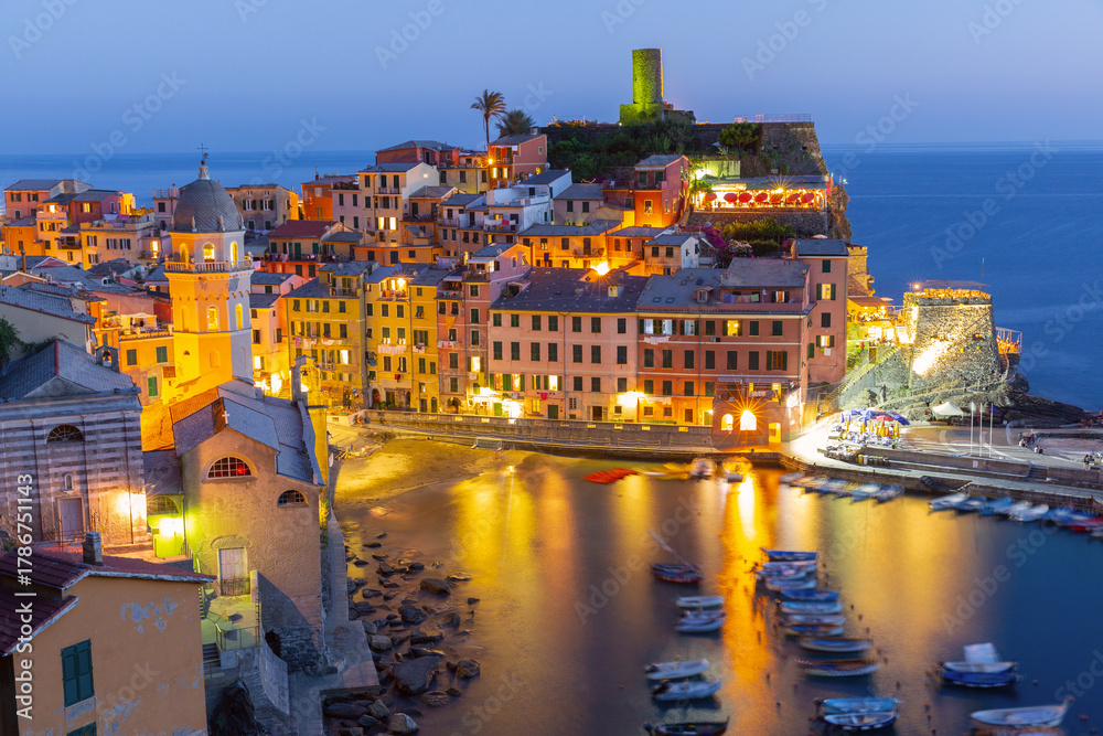 Obraz premium View of Vernazza at sunset in Liguria, Italy with illuminated harbor, boats and colorful buildings