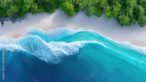 Vibrant Turquoise Ocean Waves Gently Crashing Onto A Sandy Beach Lined With Lush Green Trees Seen From A High Angle Drone View