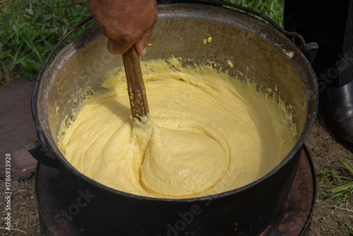  a person stirring a large batch of mămăligă, a traditional Romanian dish made from yellow maize flour. ,balmos