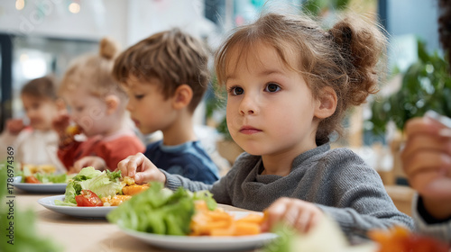 Children eating healthy lunch together in a bright room with salad and other fresh foods on their plates