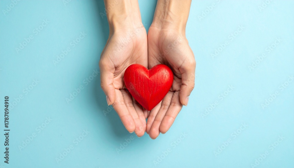 Fototapeta premium Hands Cradle a Red Heart Symbolizing Affection and Kindness on a Blue Background