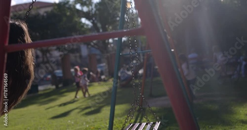 Mother on swing with infant daughter in park on sunny day - hand held shot