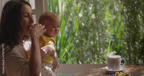 Mother drinking hot chocolate and eating at resturant with infant baby in arms