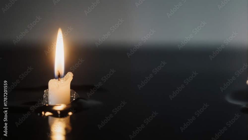 Fototapeta premium Single Lit Candle Illuminating a Dark and Reflective Surface.