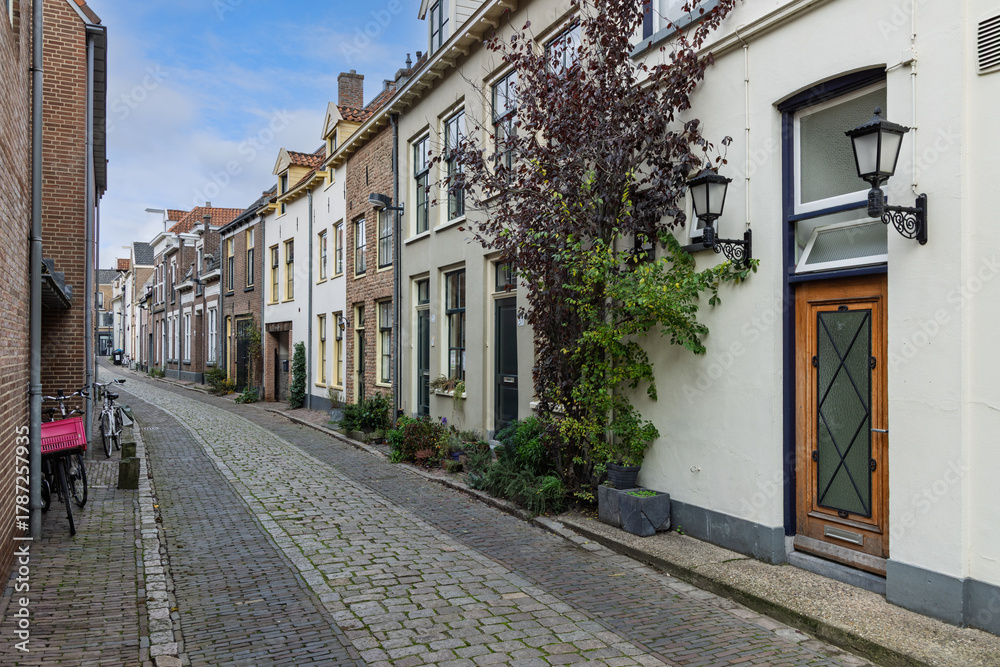 Fototapeta premium A narrow, historic cobblestone street in Zutphen, Netherlands, lined with charming traditional Dutch townhouses and classic street lanterns.