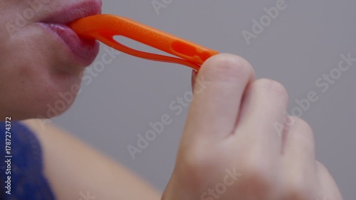 A person blows an orange plastic emergency or deterrent whistle. The whistle emits a high-pitched deterrent sound.