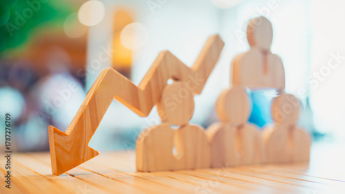 Wooden arrow pointing down over group of people icons representing workforce reduction, employee layoff, HR crisis, or economic downturn. Concept for job loss, downsizing, and business failure.