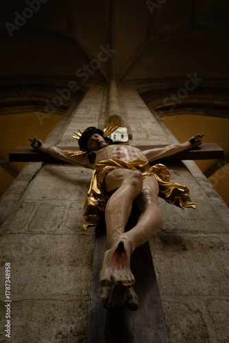Kutná Hora, Czech Republic – August 8, 2025: Dramatic low-angle view of an ornate baroque crucifix with gilded details on a Gothic pillar inside the Cathedral of Saint Barbara, Kutná Hora