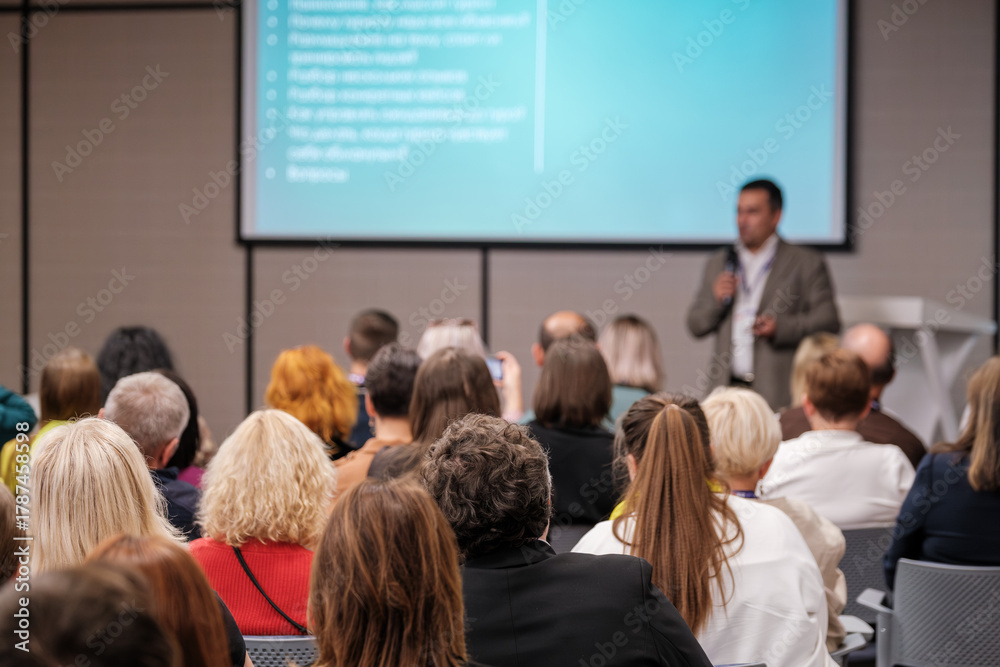 Obraz premium Audience listens to presenter during a business conference in modern meeting room with large screen