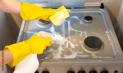Overhead view of a hand in a yellow glove vigorously scrubbing a cooktop with suds, realistic domestic cleaning action. 
