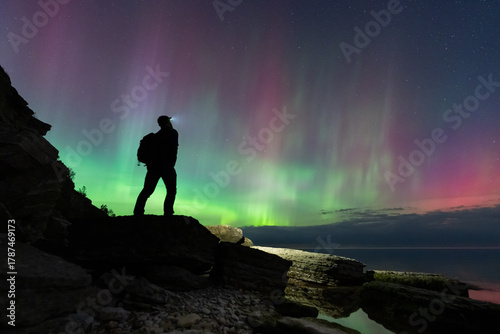 Silhouette of a hiker on a rocky cliff watching the magical Aurora Borealis, the Northern Lights, over the Baltic Sea in Estonia.