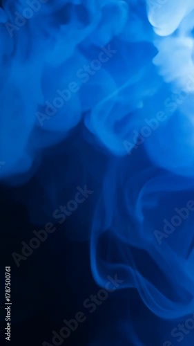 Thick blue smoke rises and curls slowly against black backdrop creating elegant swirling abstract shapes in soft motion design