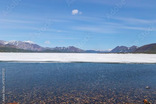 Russia, Magadan Region. Nature of Siberia and the Russian Far East. Mountain lake Malyk. Clean transparent water and unmelted ice at the beginning of summer.