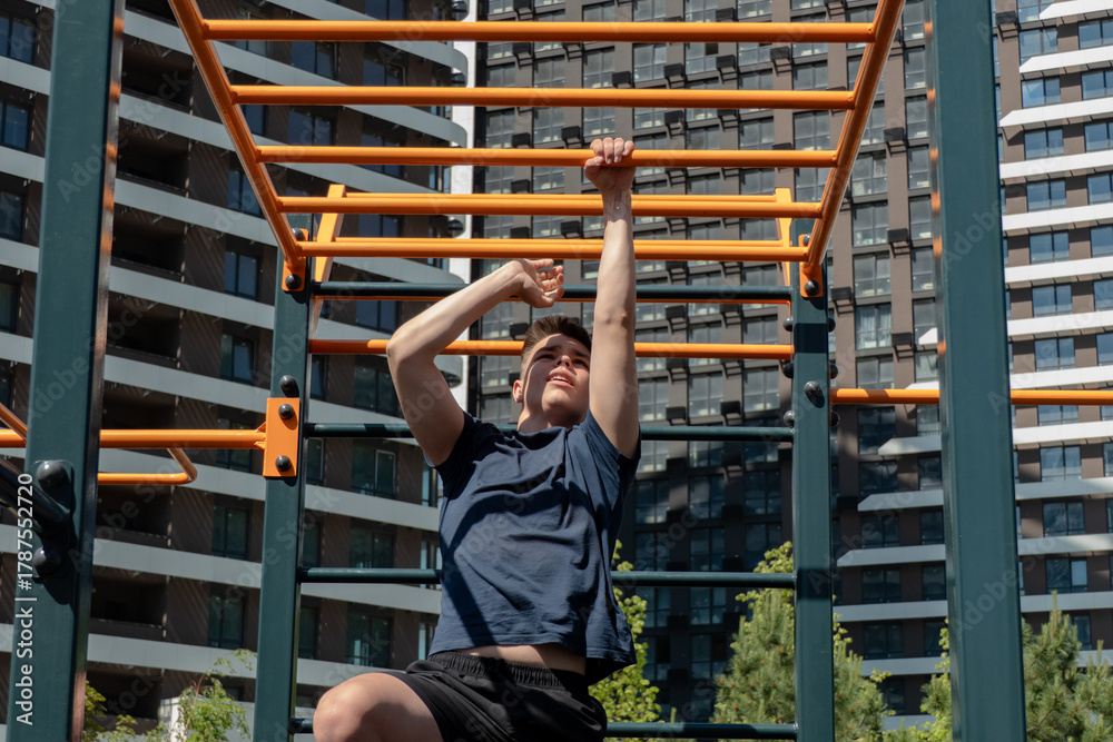Fototapeta premium Young man performing a challenging workout on monkey bars at an outdoor street workout park. Focused on fitness, strength, and active lifestyle in an urban setting.