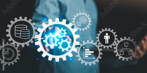 Photos A businessman interacting with virtual gear icons representing automation, workflow, data management, and corporate efficiency in digital business technology and process improvement systems