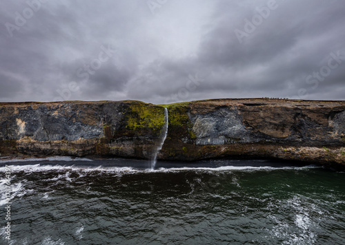 Waterfall on a rocky cliff going into the sea in Northern Iceland