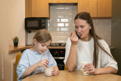 Mother and daughter enjoy eating ice cream together at a wooden table in a home kitchen, sharing a happy moment and strengthening their family relationship