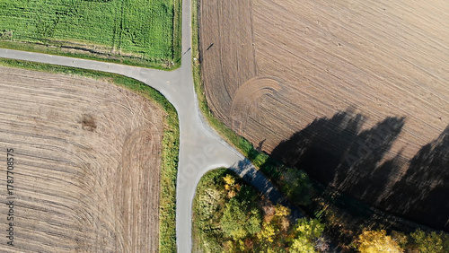 Rural road intersection showing agricultural fields, green growth, plowed soil, and autumn trees from aerial view
