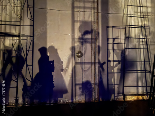 Fotografie Shadows of ballet dancers and stage crew projected on a backstage wall under dramatic lighting, creating artistic silhouettes and geometric ladder patterns in a theater performance setting
