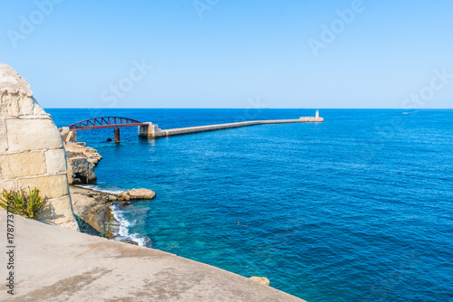 Papier peint Rocky beach near pedestrian bridge and breakwater in turquoise sea, Valletta MAL