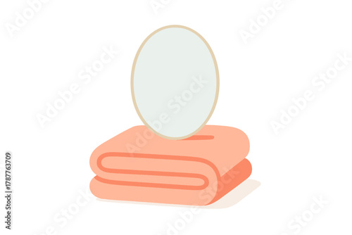 Oval vanity mirror resting on stack of folded peach colored towels