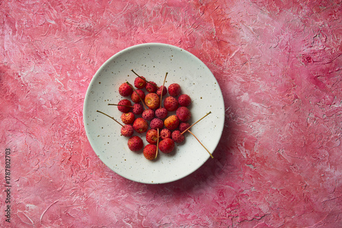 Exotic pink lychees with stem, in a speckled ceramic bowl on a heavily textured, custom made red and pink surface.