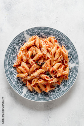 A plate of mezze penne with tomato sauce, garnished with a sprinkle of freshly grated Parmigiano Reggiano on a light background.