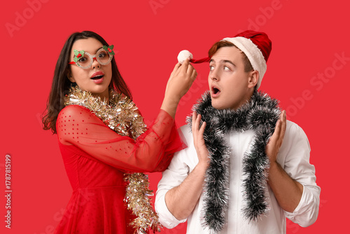 Young couple with Christmas tinsel on red background
