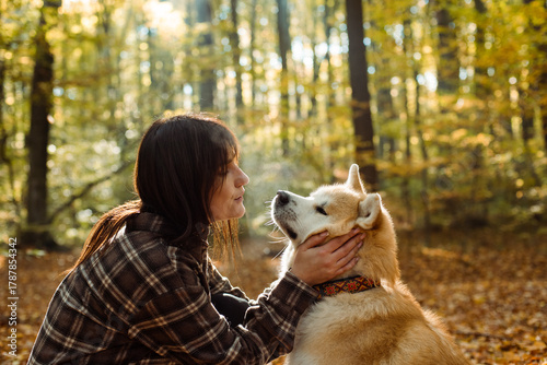 young woman walking and playing with her japanese akita puppy in autumn forest