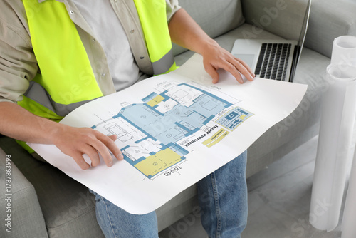 Male contractor with house plan sitting on sofa in room, closeup
