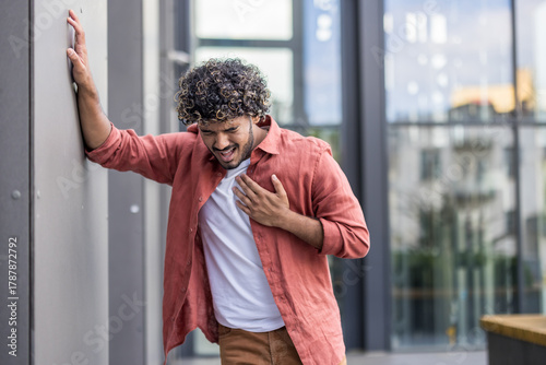 Valokuva A young Indian man stands outside, grimacing in pain and holding his hand over h