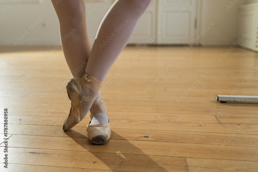 Naklejka premium Worn ballet pointe shoes on feet in dance class. Well worn pointe shoes of ballet dancer. Classical ballerina woman in dance studio. Classical pointe shoes for dance training. Ballet school concept