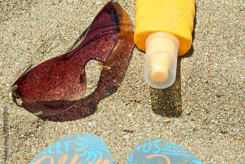 Top view of sunglasses, sunscreen bottle on sand
