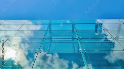 Modern glass and steel tower architecture of a building under construction against a clear blue sky with white clouds
