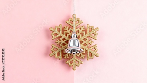 Golden snowflake ornament with silver bell decoration on soft pink background. Holiday minimal concept.